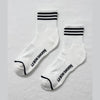 White socks with black stripes and 'Le Bon Shoppe' branding on a light gray background