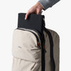 Person placing a black item into a light ash backpack on a white background