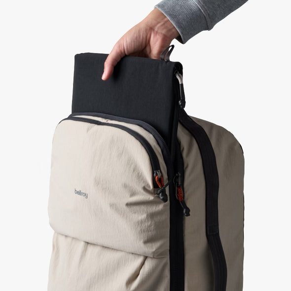 Person placing a black item into a light ash backpack on a white background
