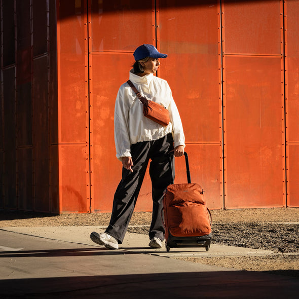 Person walking with a Lite Carry-On 38L by Bellroy in clay against an orange wall
