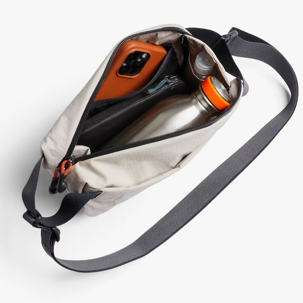 Open beige crossbody bag with phone, water bottle, and other items on a white background