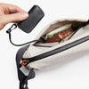 Hand holding a black key case above an open beige bag with travel items.