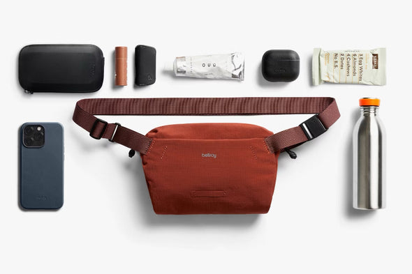 Collection of travel essentials including a red waist bag, phone, water bottle, and other items on a white background.