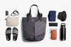 Collection of travel or daily essentials including a tote bag, slippers, water bottle, and pouches on a white background.