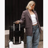 Woman holding a black bag over a white suitcase with a dark background