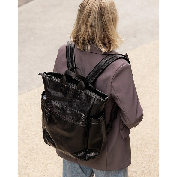 Person wearing a black backpack on a neutral background