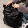 Person opening a black leather bag outdoors