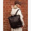 Person wearing a brown cap and carrying a black backpack against a brick wall.