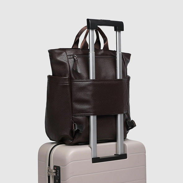 Brown leather backpack with wheels on a beige suitcase against a light gray background