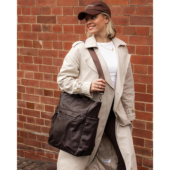 Woman holding a brown leather bag against a brick wall