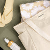 Beige tote bag with floral towel and skincare bottle on a green surface