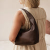 Woman wearing a brown leather shoulder bag with a neutral background