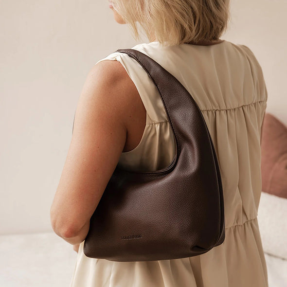 Woman wearing a brown leather shoulder bag with a neutral background