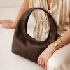 Brown handbag held by a person wearing a gold watch on a light background