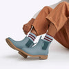 Light blue rain boots with brown soles worn by a person in brown pants and striped socks.