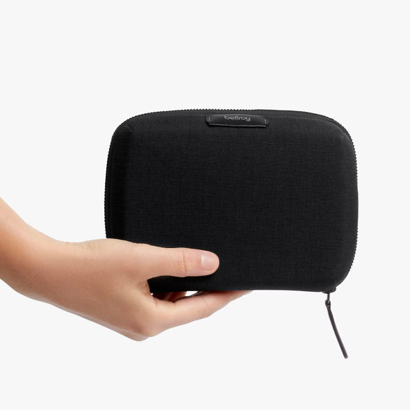 Black zippered pouch held by a hand on a white background