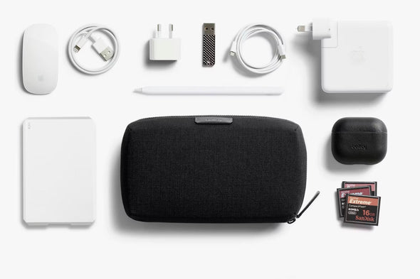Collection of electronic accessories including a black Tech Kit by Bellroy, power adapter, and memory cards on a white background.