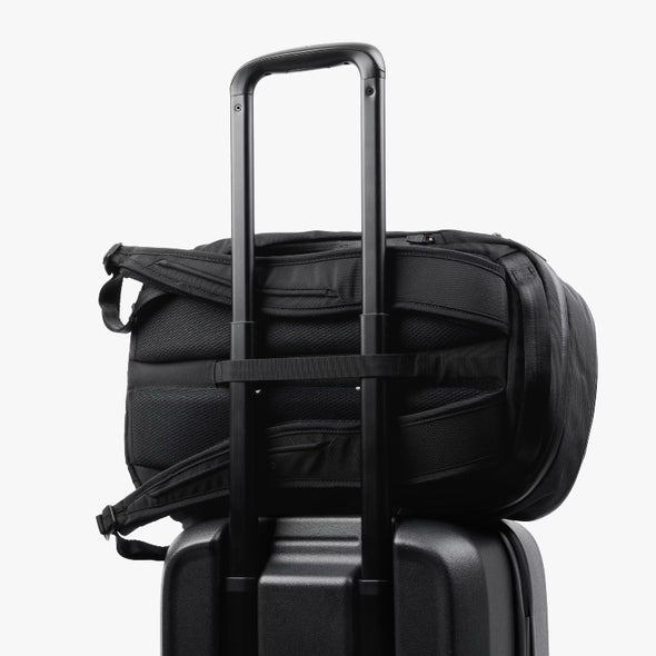 Black duffel bag on top of a suitcase with a white background