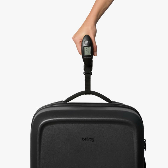 Black suitcase with a digital luggage scale attached, held by a hand on a white background.