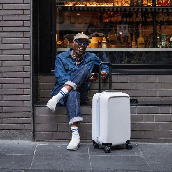 Man sitting on a step with a white suitcase next to him, in front of a bar.