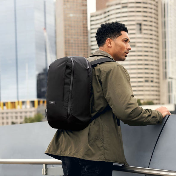 Man with a black backpack standing on a rooftop with city skyline in the background