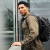Man wearing a green jacket and black backpack against a blurred background