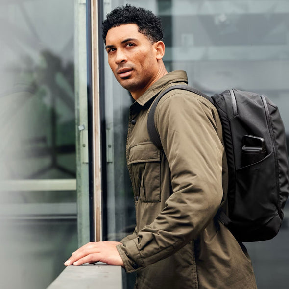 Man wearing a green jacket and black backpack against a blurred background
