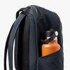 Navy backpack with an orange water bottle in a front pocket on a white background