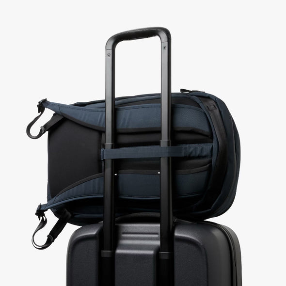 Navy backpack with a shoulder strap over a suitcase on a white background