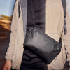Person wearing a beige jacket with a black bag over their shoulder outdoors.