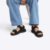 Person wearing black sandals with straps on a white background