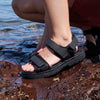 Person wearing black sandals with straps by a body of water