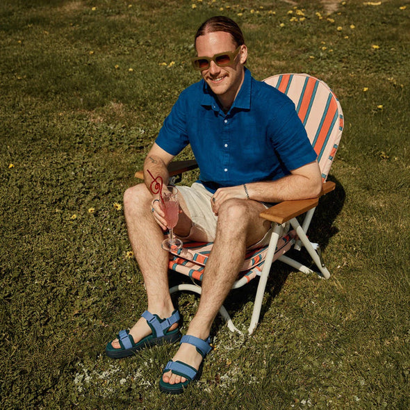 Man sitting on a striped chair outdoors, holding a drink.