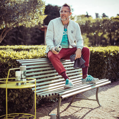 Man sitting on a bench in a park with trees and greenery in the background